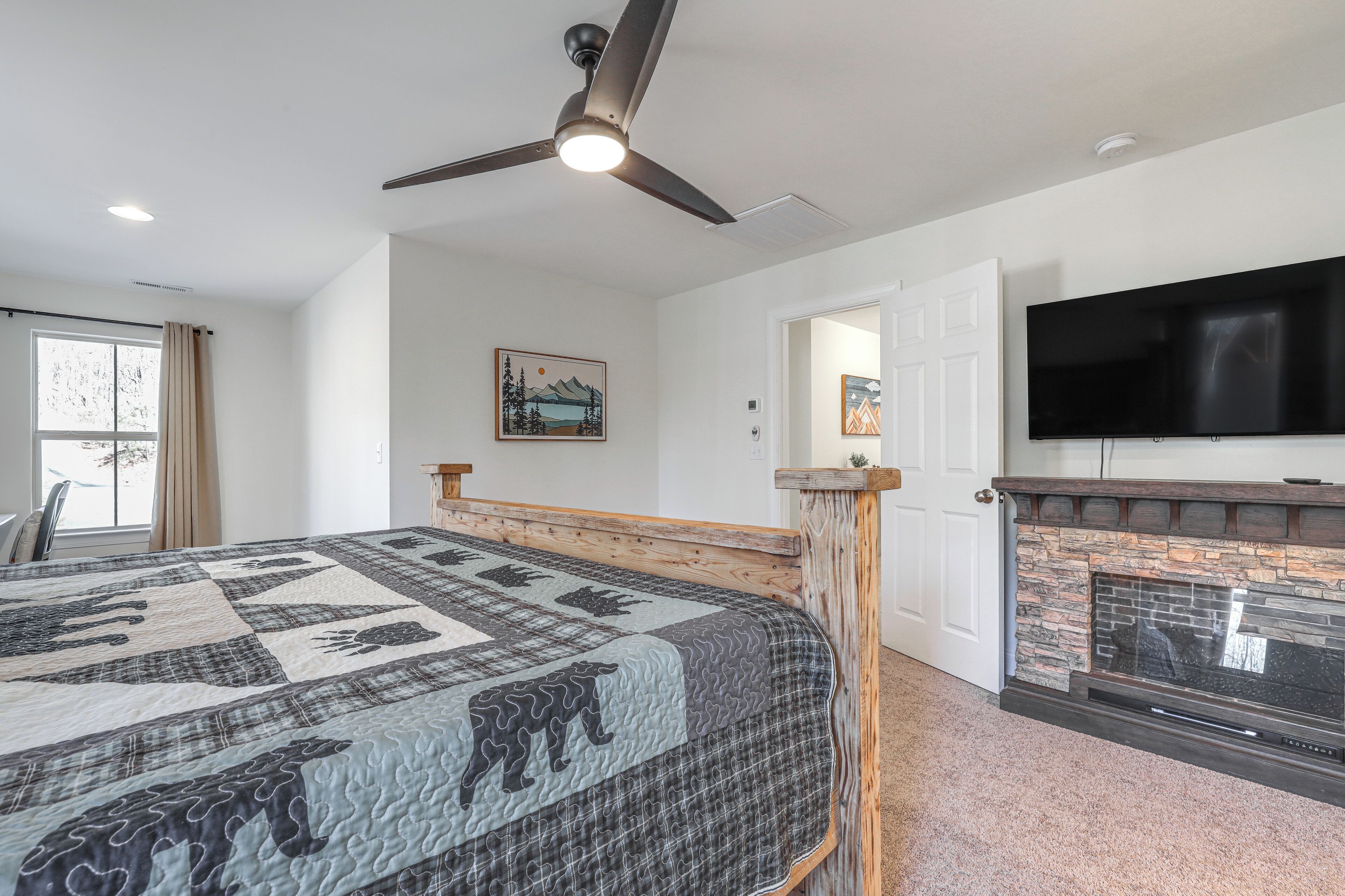 A bedroom with a large bed, a fireplace, a ceiling fan, and a TV mounted on the wall.