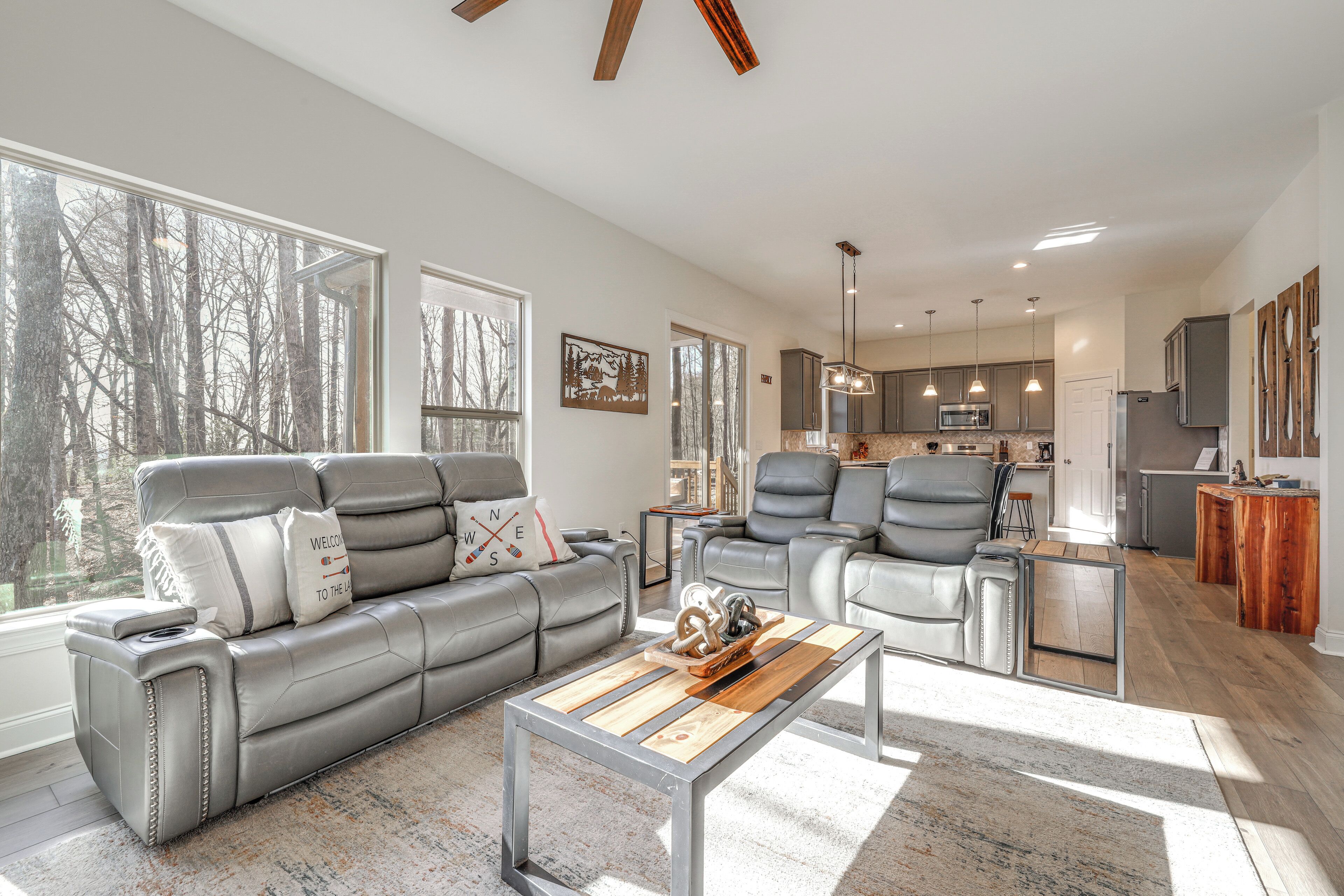 A modern living room with a grey leather sofa, a wooden coffee table, and a view of the kitchen in the background.