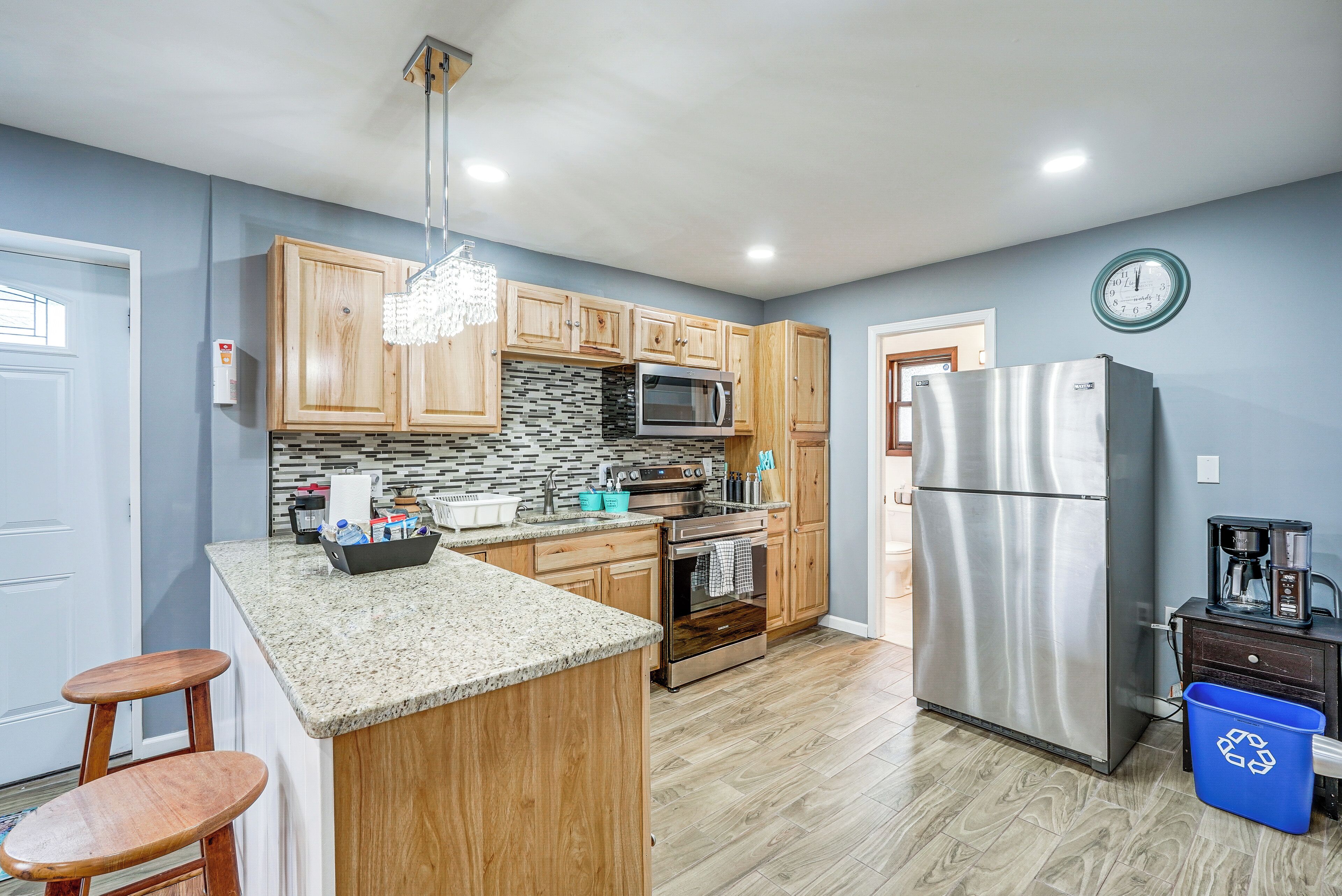 A kitchen with wooden cabinets, a granite countertop, stainless steel appliances, and a blue recycling bin.