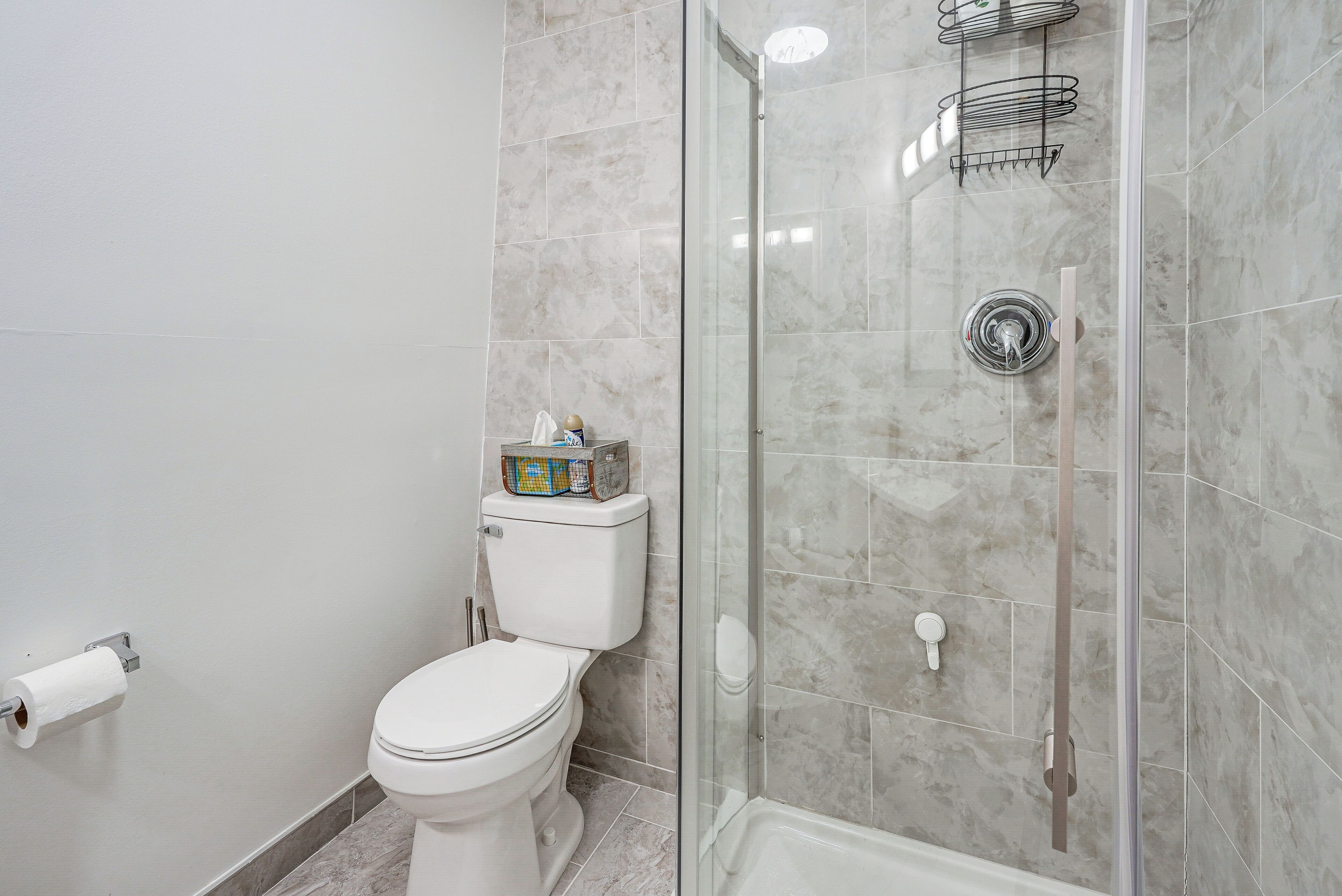 Un baño con inodoro, ducha con cerramiento de vidrio y pared con mosaicos de mármol.
