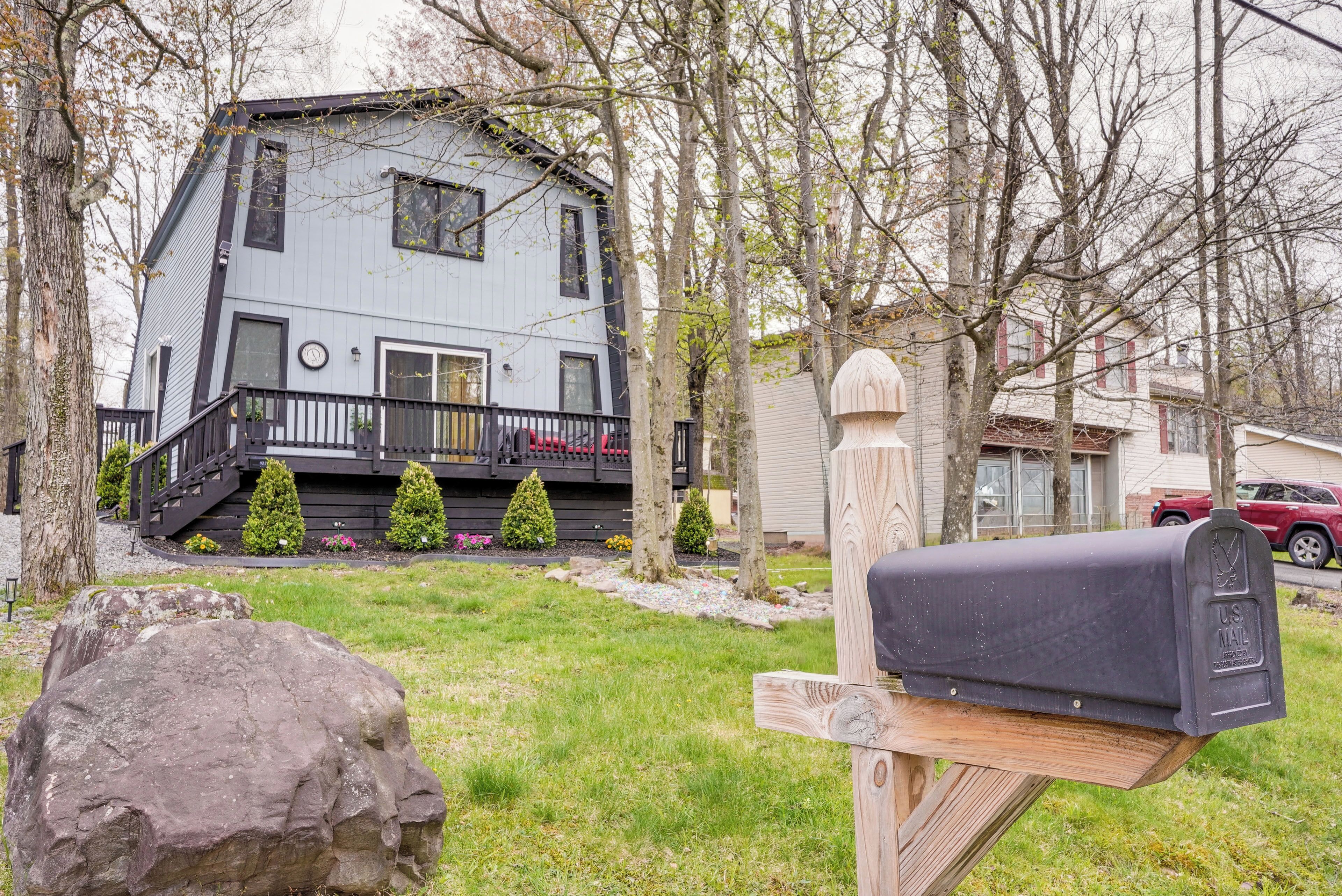 A two-story house with a front porch, mailbox, and a large rock in the foreground.