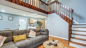 A living room with a grey sectional sofa, a wooden staircase, and a kitchen in the background. - Family Getaway w/ Deck Near Tobyhanna State Park (Tobyhanna)