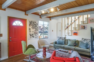 Una sala de estar con una puerta roja, una silla verde, un sillón color beige y un sofá azul, además de una alfombra estampada.