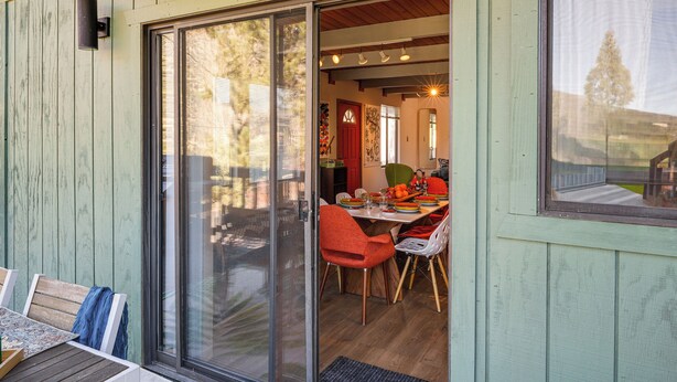 Un comedor con mesa y sillas, un ventanal corredero que da a un espacio interior y una pared exterior de madera.