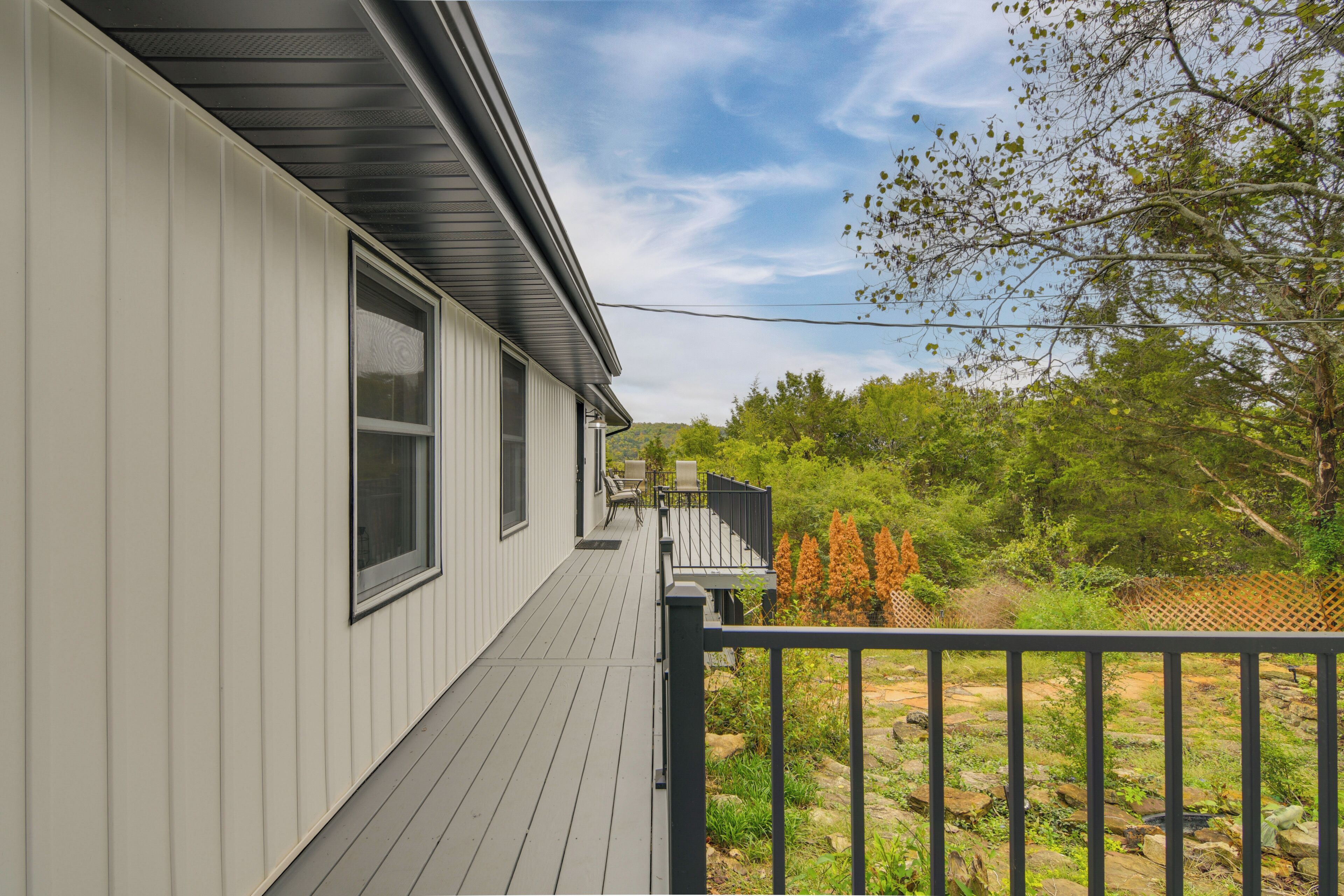 A house with a deck, a fenced yard, and a view of trees and shrubs.