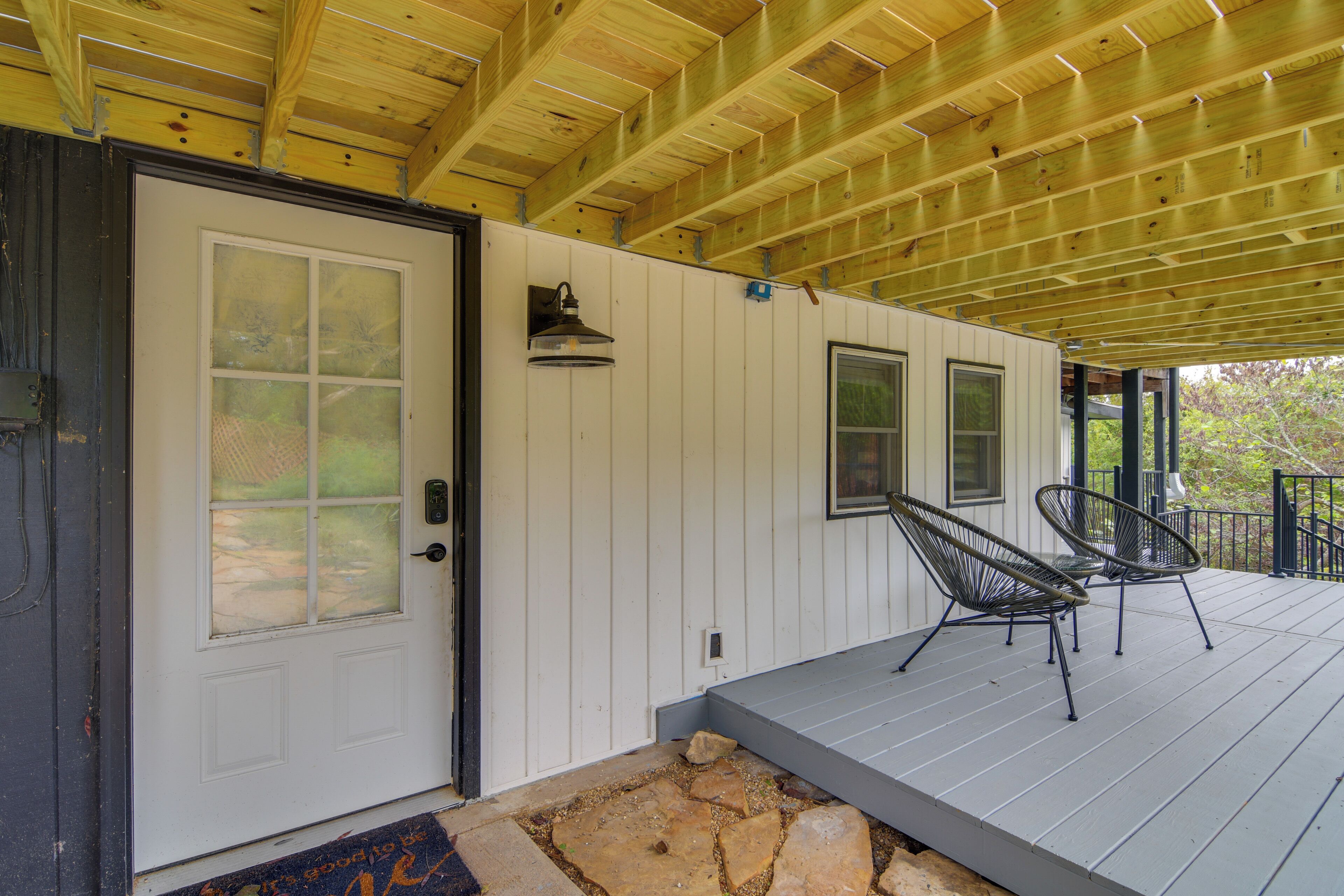 A covered porch with a wooden ceiling, a white door, and two metal chairs.
