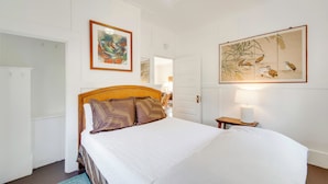 A bedroom with a large bed, a wooden headboard, and a nightstand with a lamp. There is a door leading to another room and a wall-mounted artwork above the bed. - Lush Island Oasis Near Volcanoes National Park (Volcano)
