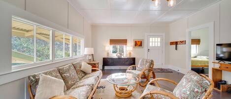 A spacious living room with a sofa, chairs, a glass coffee table, and a TV.