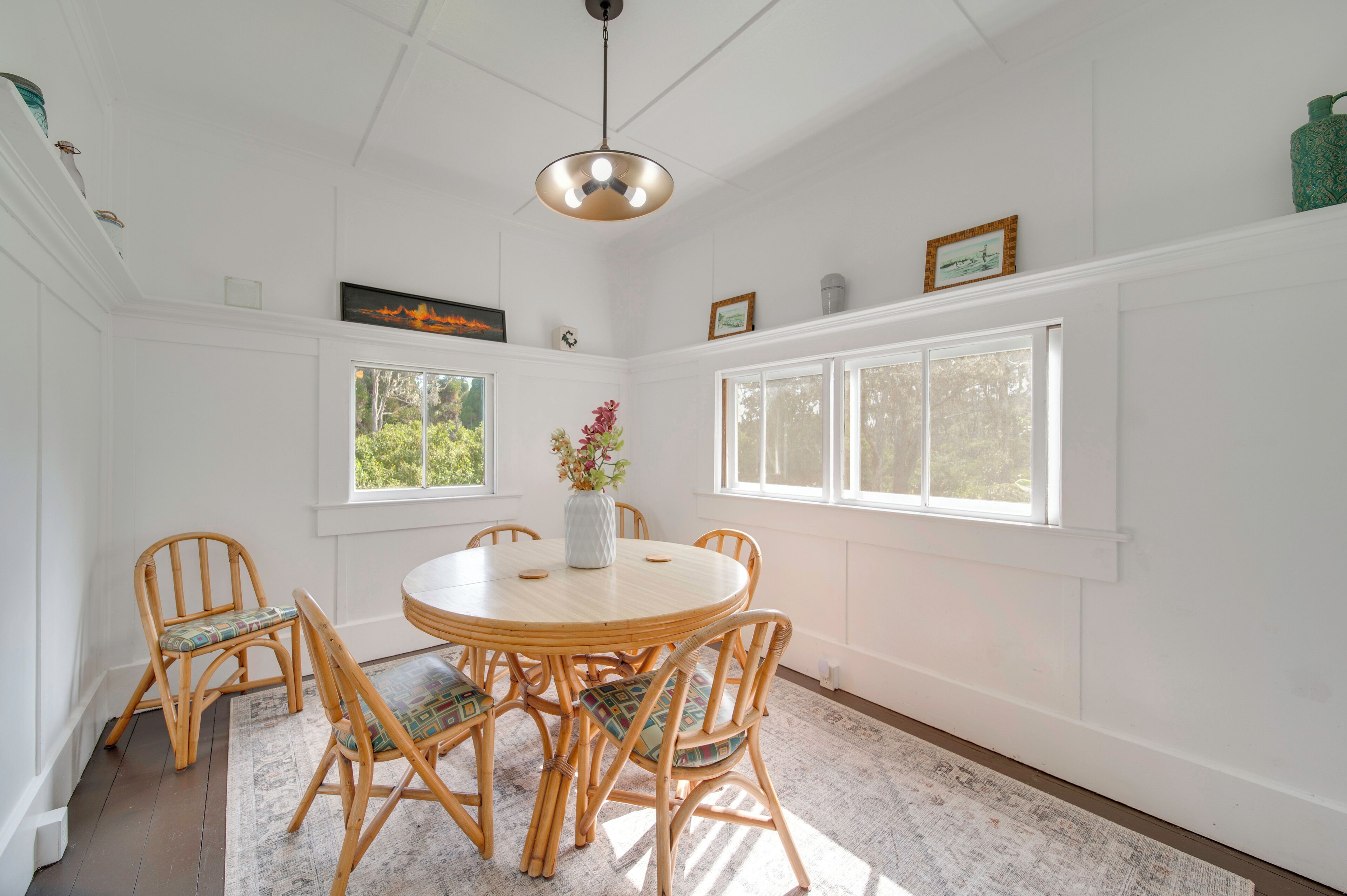 A dining area with a round wooden table surrounded by six wicker chairs, a vase with flowers, and a pendant light.