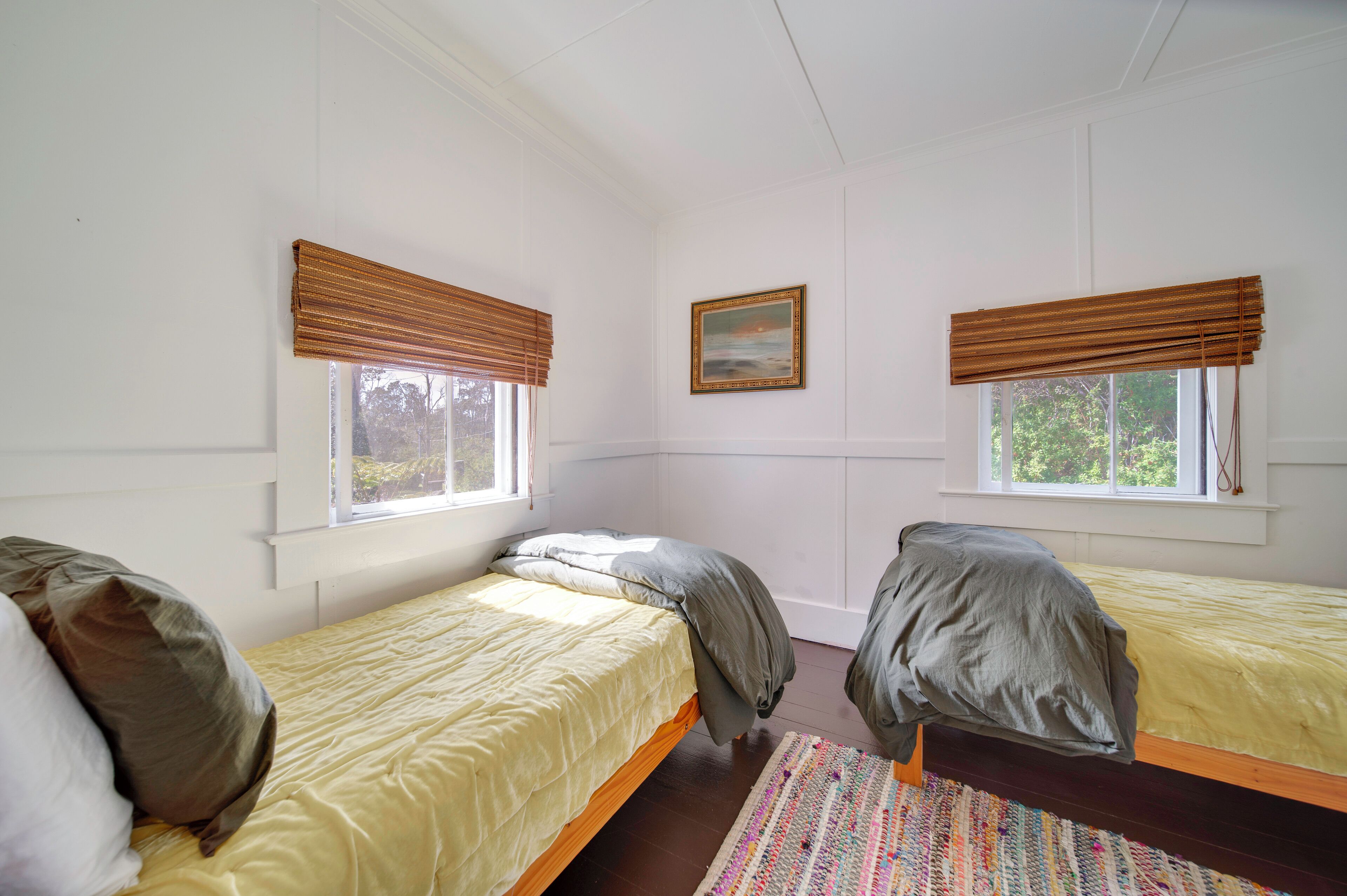 A room with two single beds, each with a window and a painting on the wall.