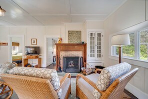 A living room with wicker furniture, a fireplace, a television, and a window with a view of greenery. - Lush Island Oasis Near Volcanoes National Park (Volcano)