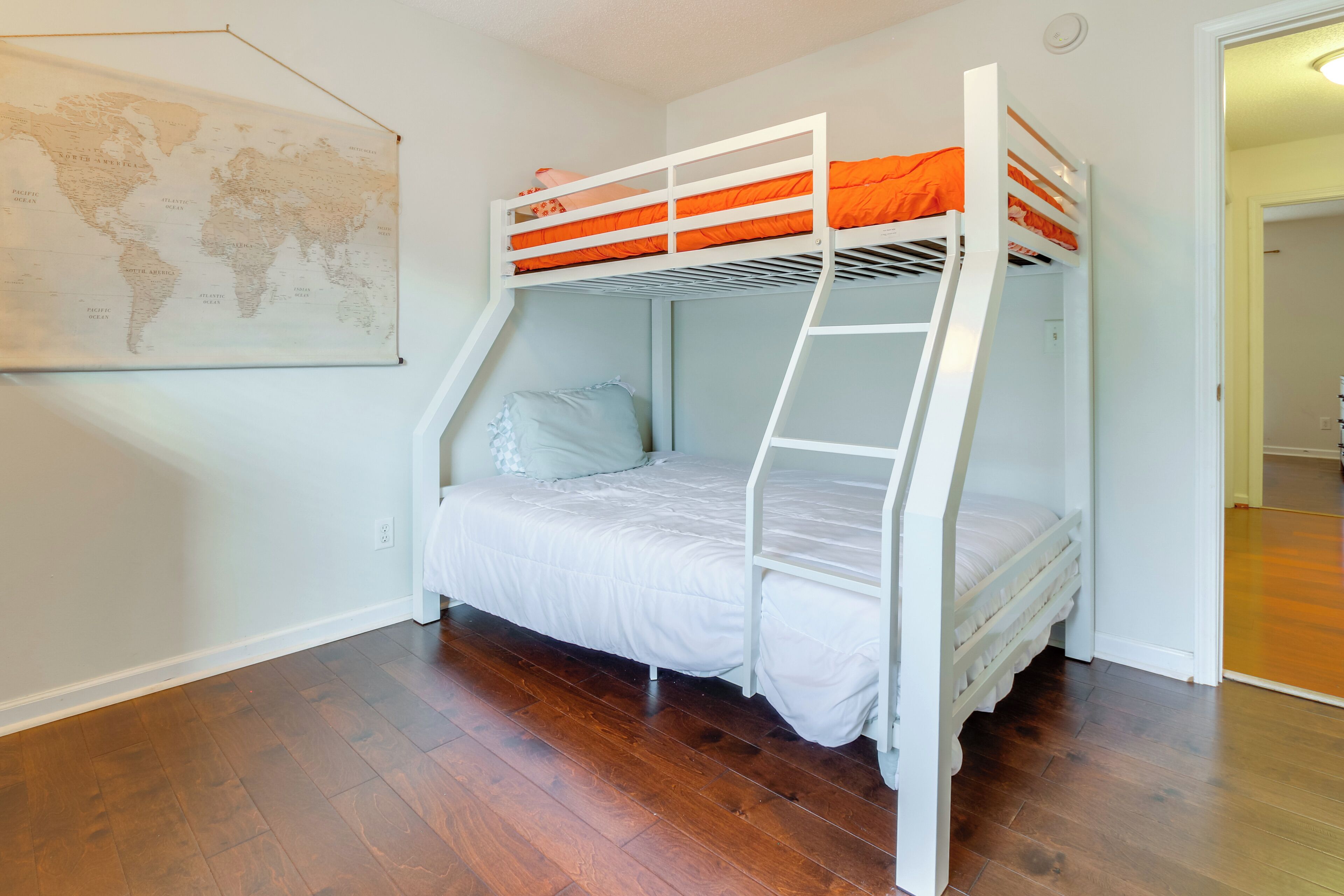 A bunk bed room with a world map on the wall, wooden flooring, and a ladder.