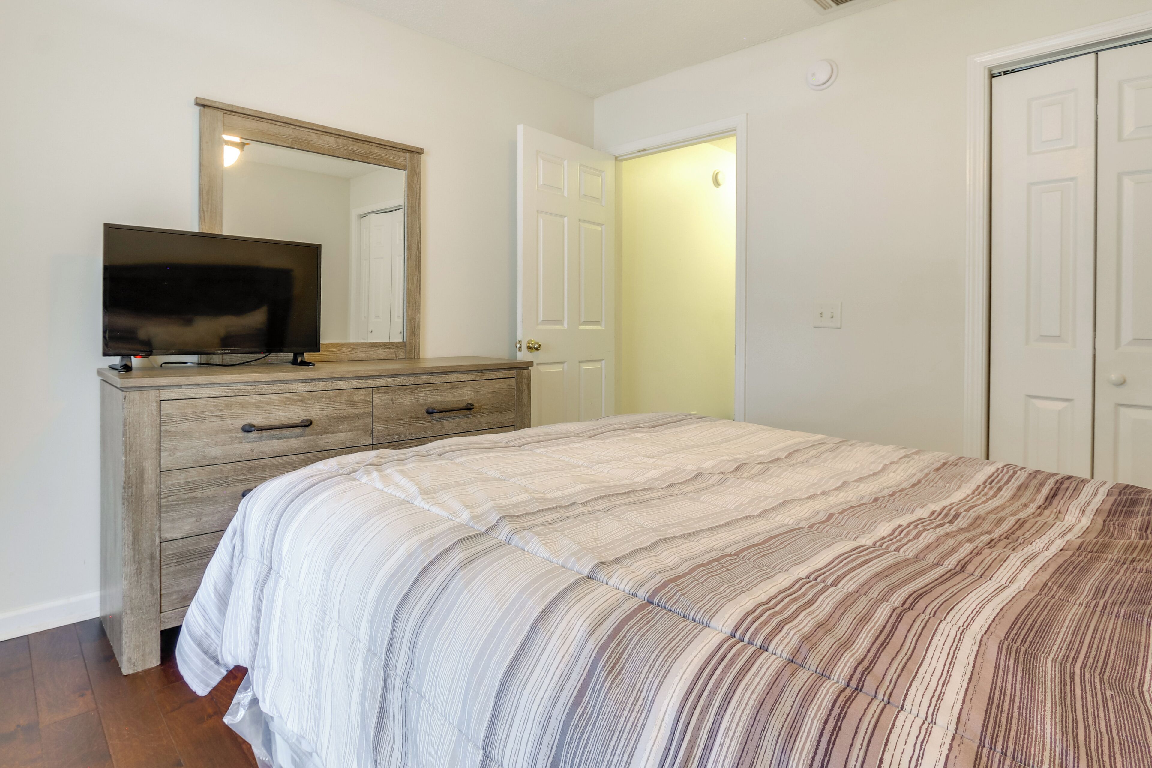 A bedroom with a bed, a dresser, a television on the dresser, and a door leading to another room.