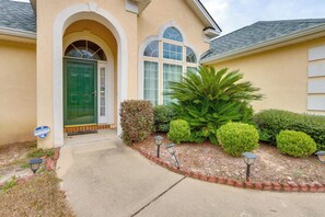 A house with a green door, a covered porch, and a well-maintained garden with a palm tree and shrubs. - 11 Mi to Savannah! Suburban Home w/ Spacious Yard (Pooler)