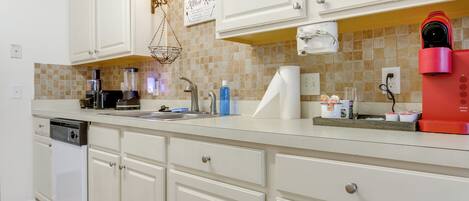 A kitchen with white cabinets, a tiled backsplash, a coffee maker, and a dishwasher.