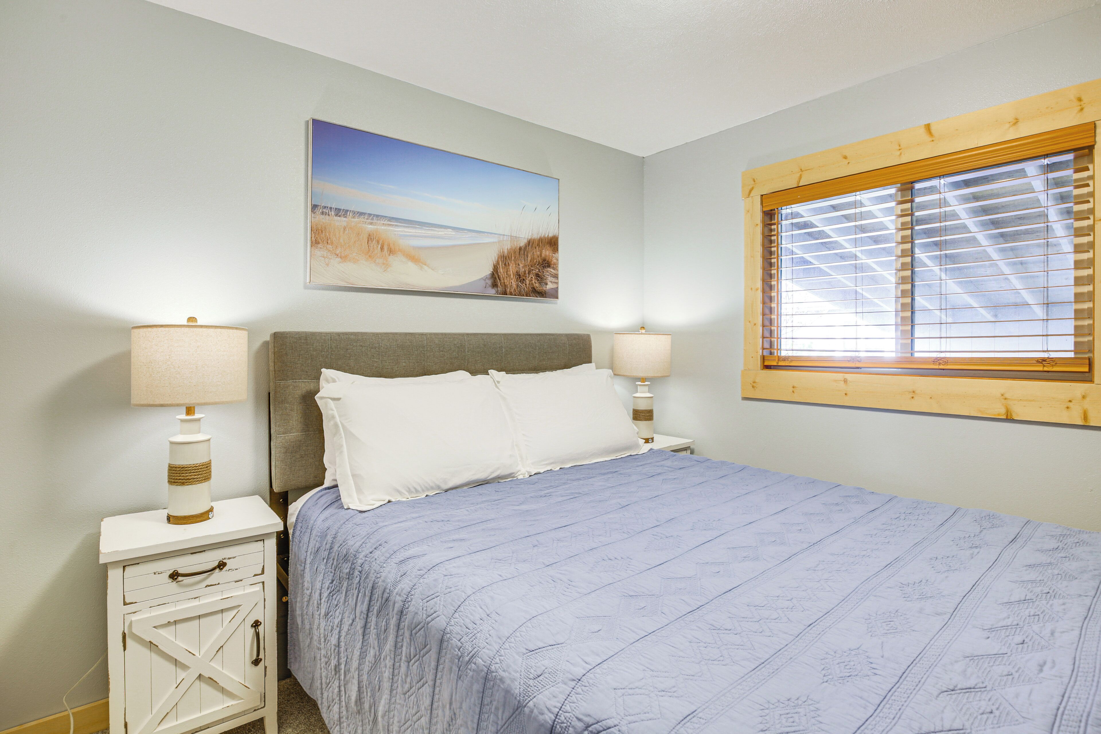 Een slaapkamer met een bed, twee nachtkastjes met lampen, een raam met zonwering en een decoratie met een strandthema.