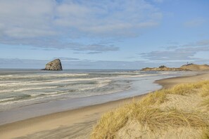 Une plage avec des dunes de sable et une grande formation rocheuse dans l’eau.