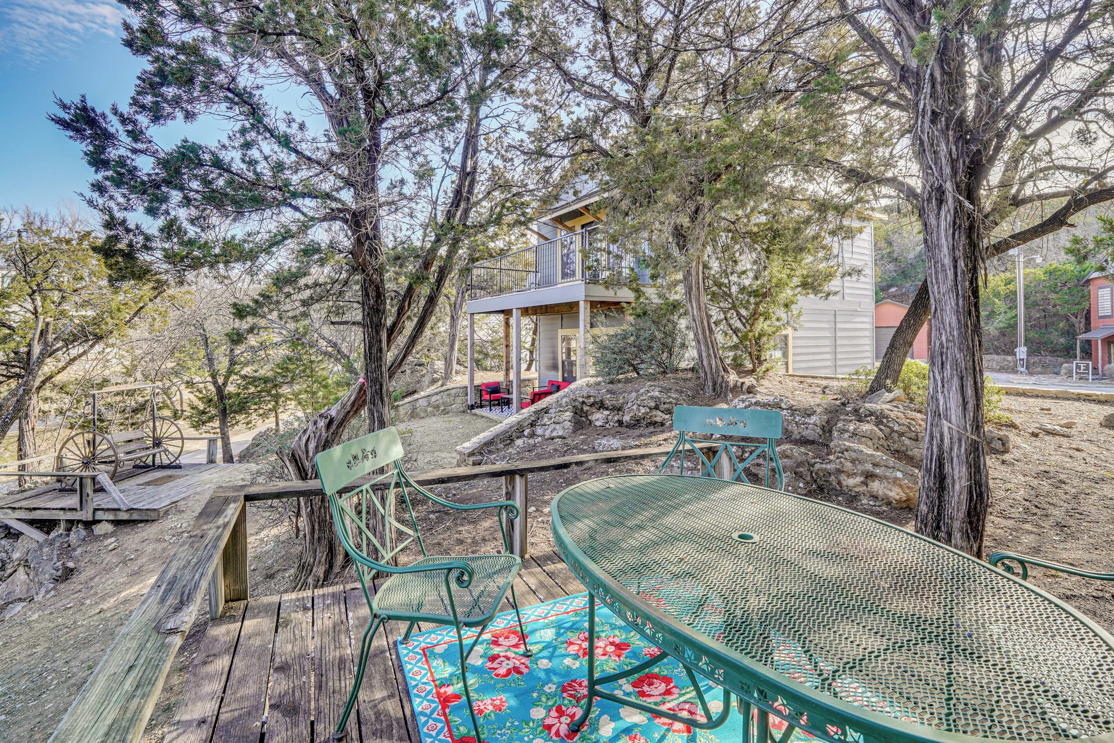 Un espace extérieur aménagé dans un style rustique, avec une table et des chaises en métal, entouré d’arbres et doté d’une terrasse en bois.