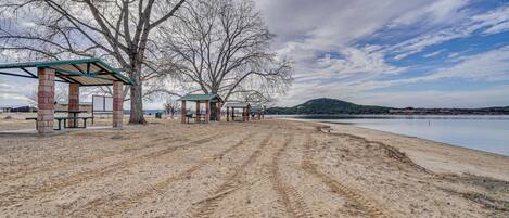 A sandy beach with picnic shelters and a lake in the background.