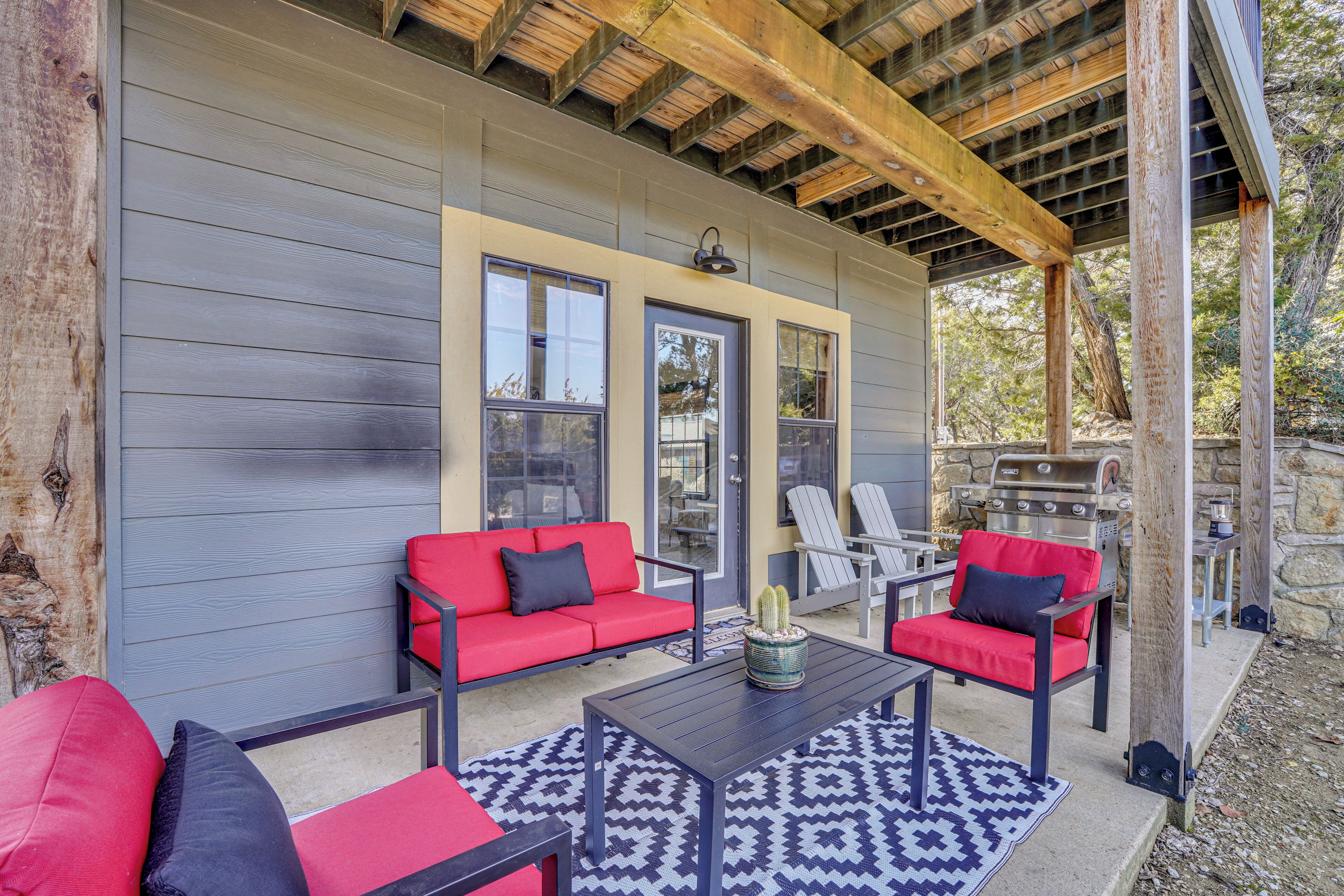 A covered patio area with a gray exterior wall, two red sofas with black cushions, a black table, and a patterned rug.