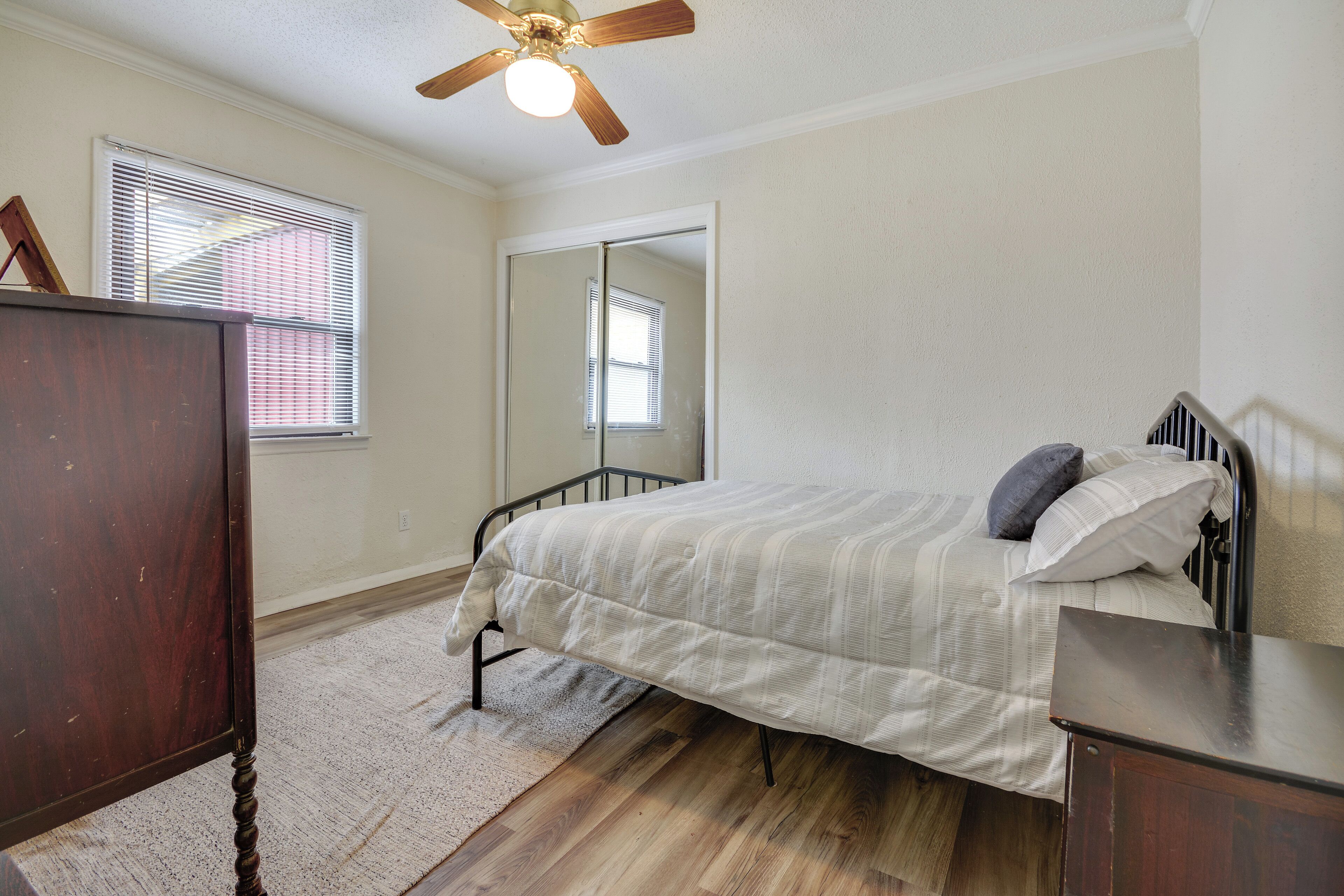 A bedroom with a bed, a dresser, a mirror, and a ceiling fan.