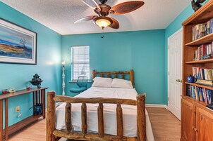 Un dormitorio con una cama de madera, un ventilador de techo, una estantería y un cuadro en la pared.