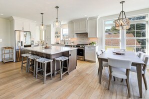 A modern kitchen with a central island, bar stools, a dining table with chairs, and pendant lighting. - Family Friendly! Canal-front Gem in Bethany Beach (Bethany Beach)