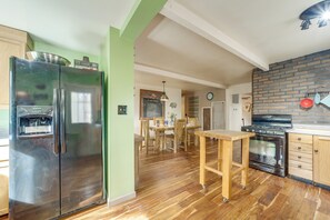 Eine Küche mit einem Edelstahlkühlschrank, einem Holztisch und einer Küchenwand aus Backsteinen.