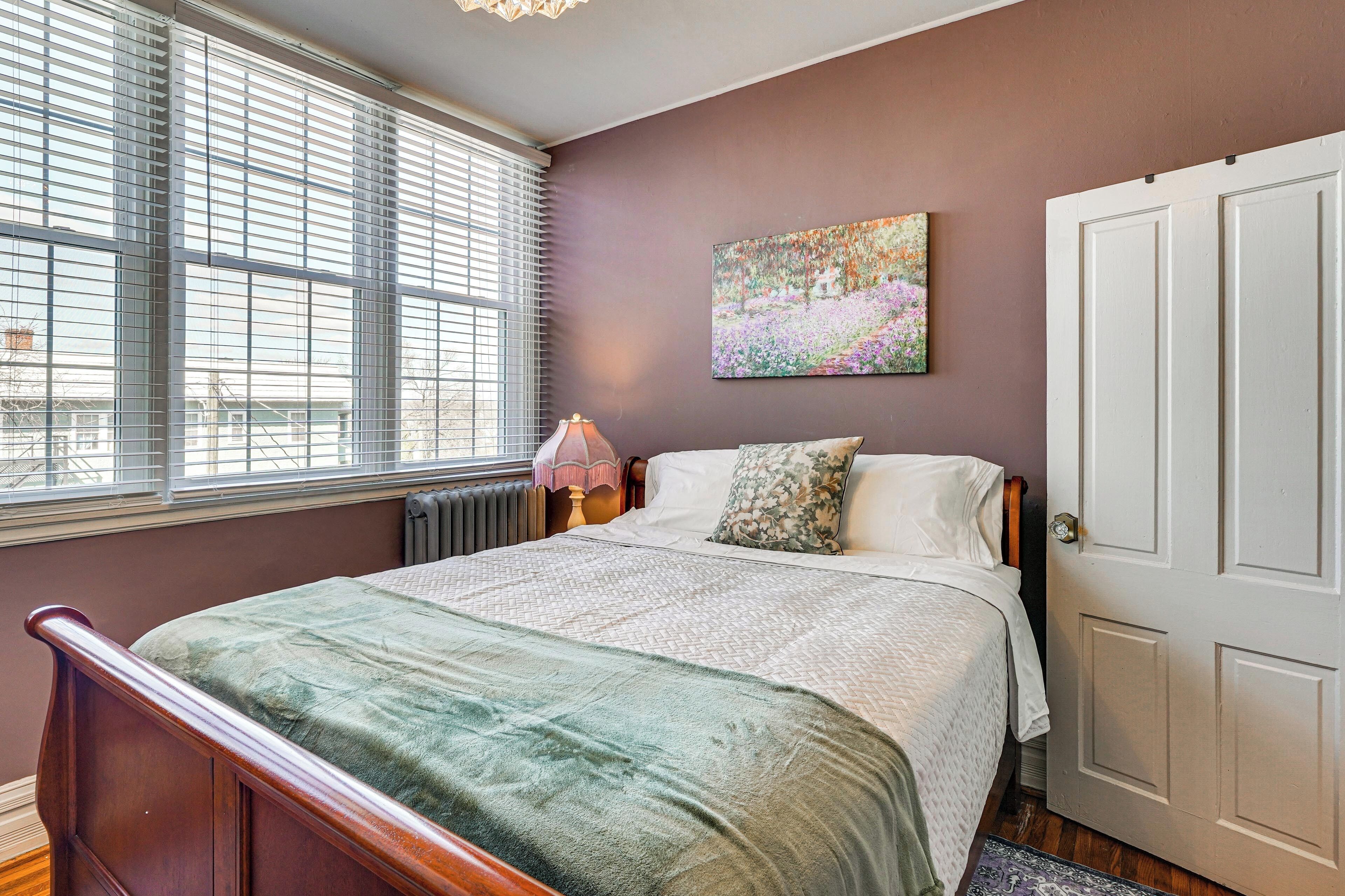 Ein Schlafzimmer mit Bett, Fenster mit Jalousien, Heizkörper, Lampe und Tür.