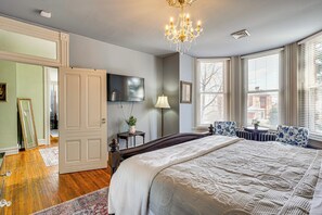 Een slaapkamer met een groot bed, een kroonluchter, een televisie en een raam met luxaflex.