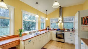 A kitchen with white cabinets, a wooden countertop, a stove, and a refrigerator. There are windows with white frames and a view of trees outside. - Walk to Irondale Beach Park! Family Haven w/ Yard (Port Hadlock)