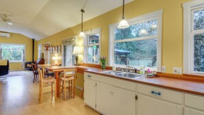 A kitchen with wooden cabinets, a large window, and a dining area with chairs. - Walk to Irondale Beach Park! Family Haven w/ Yard (Port Hadlock)