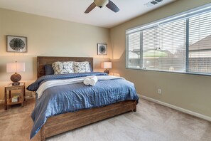 Quarto com cama de madeira, duas luminárias de cabeceira, ventoinha no teto e uma grande janela com persianas.