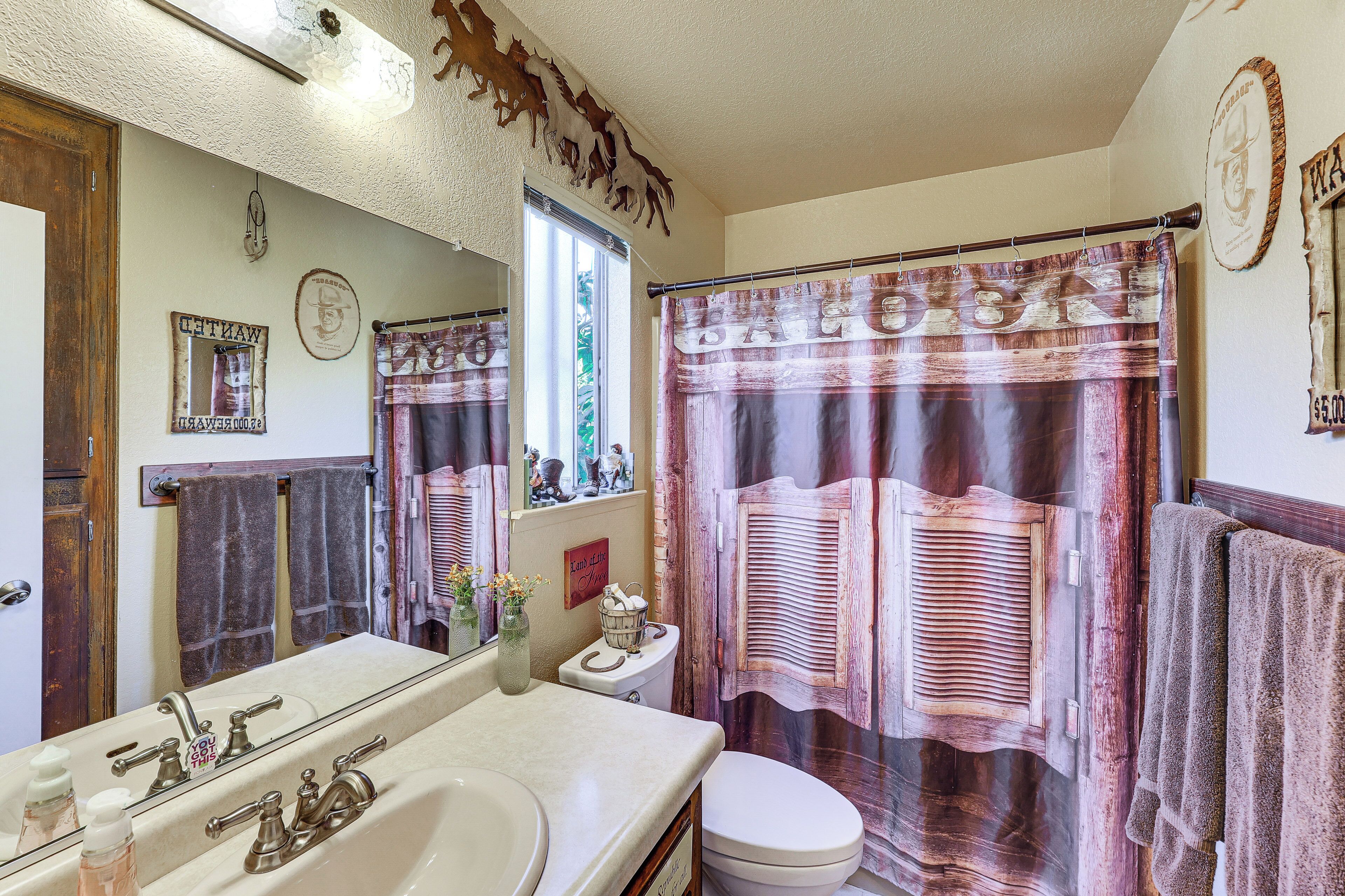 Une salle de bain avec un grand miroir, un lavabo avec un robinet, des toilettes et un rideau de douche, avec une serviette suspendue sur le côté droit.