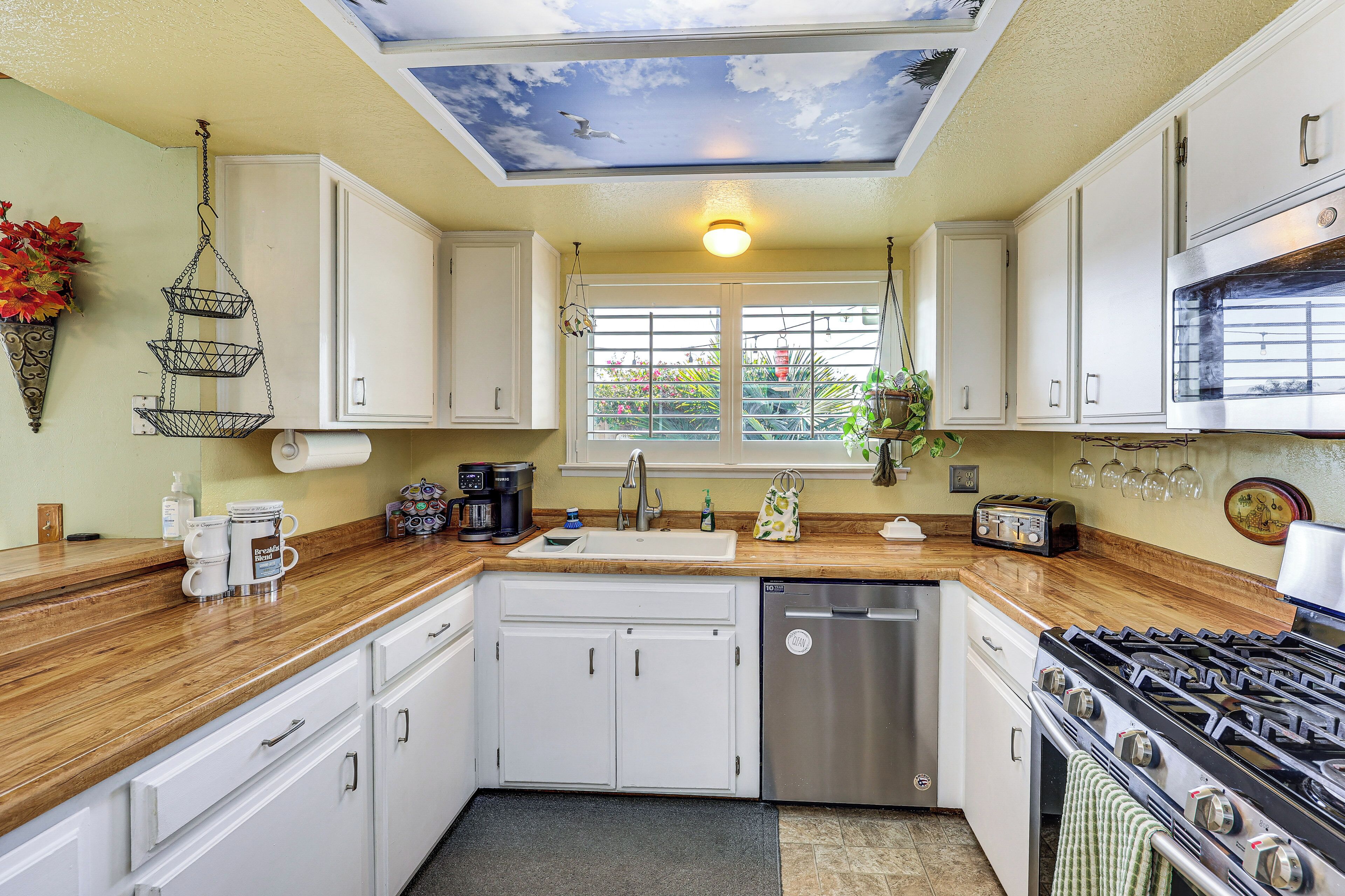 A kitchen with white cabinets, a stainless steel dishwasher, a gas stove, and a ceiling mural.