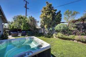 Ein Garten mit Whirlpool, Holzlattenzaun und unterschiedlichen Pflanzen und Bäumen.