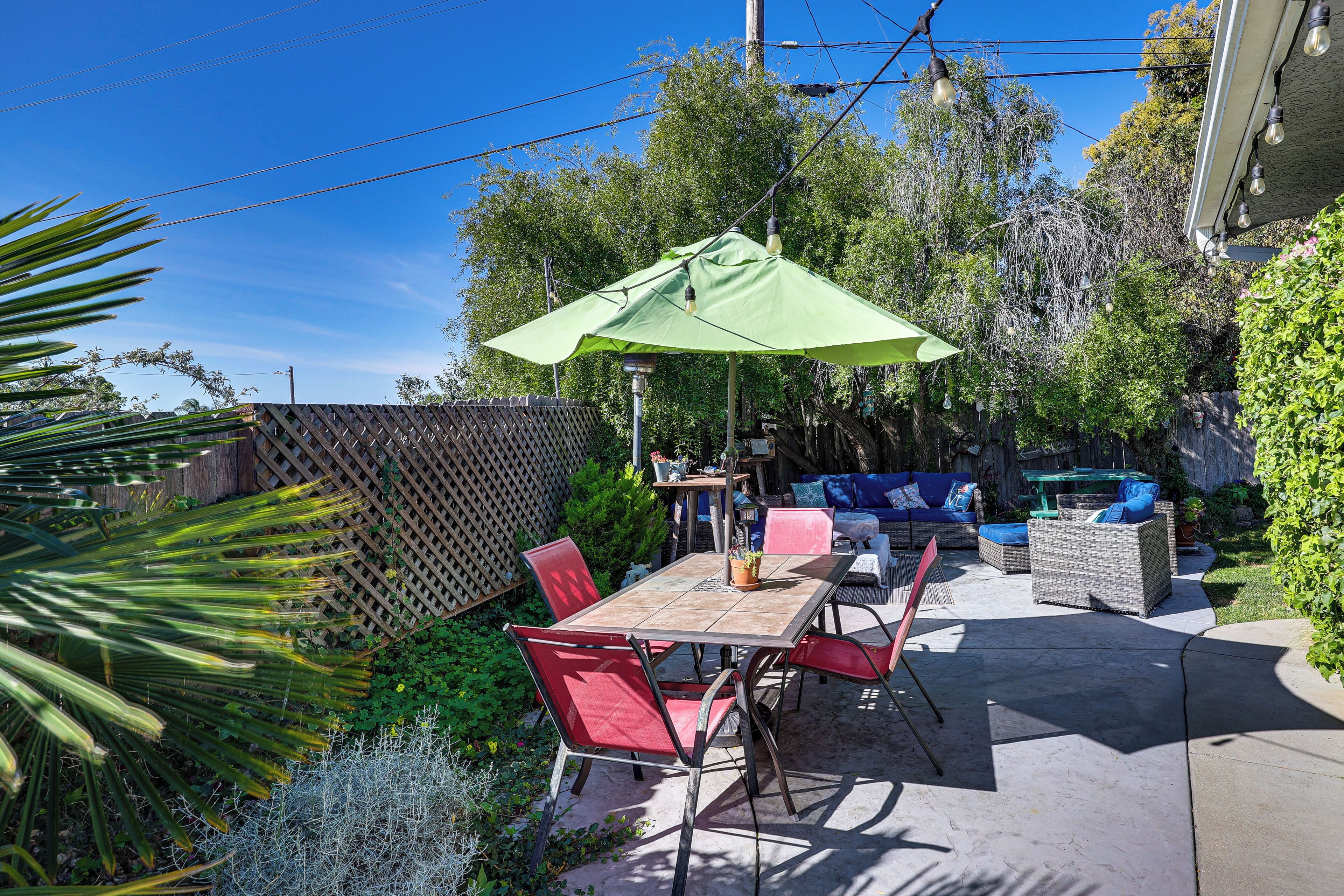 An outdoor patio with a table and chairs, a green umbrella, wicker furniture, and a wooden fence.