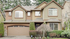 A two-story house with a garage, a covered driveway, and a well-maintained front yard with shrubs and a tree. - Gateway to Greater Seattle! Spacious, Modern Home (Bothell)