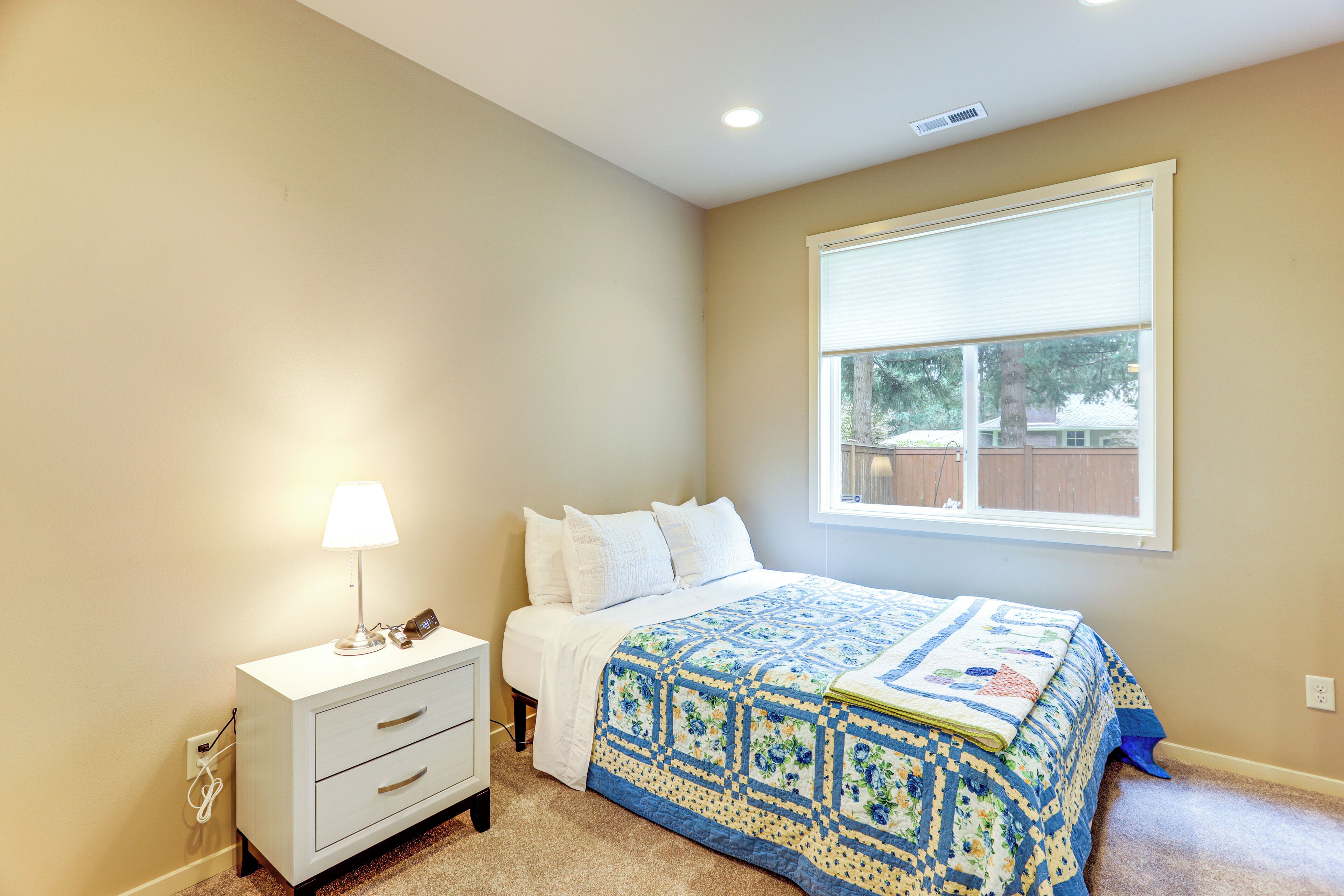 A bedroom with a bed, bedside table, lamp, and window.