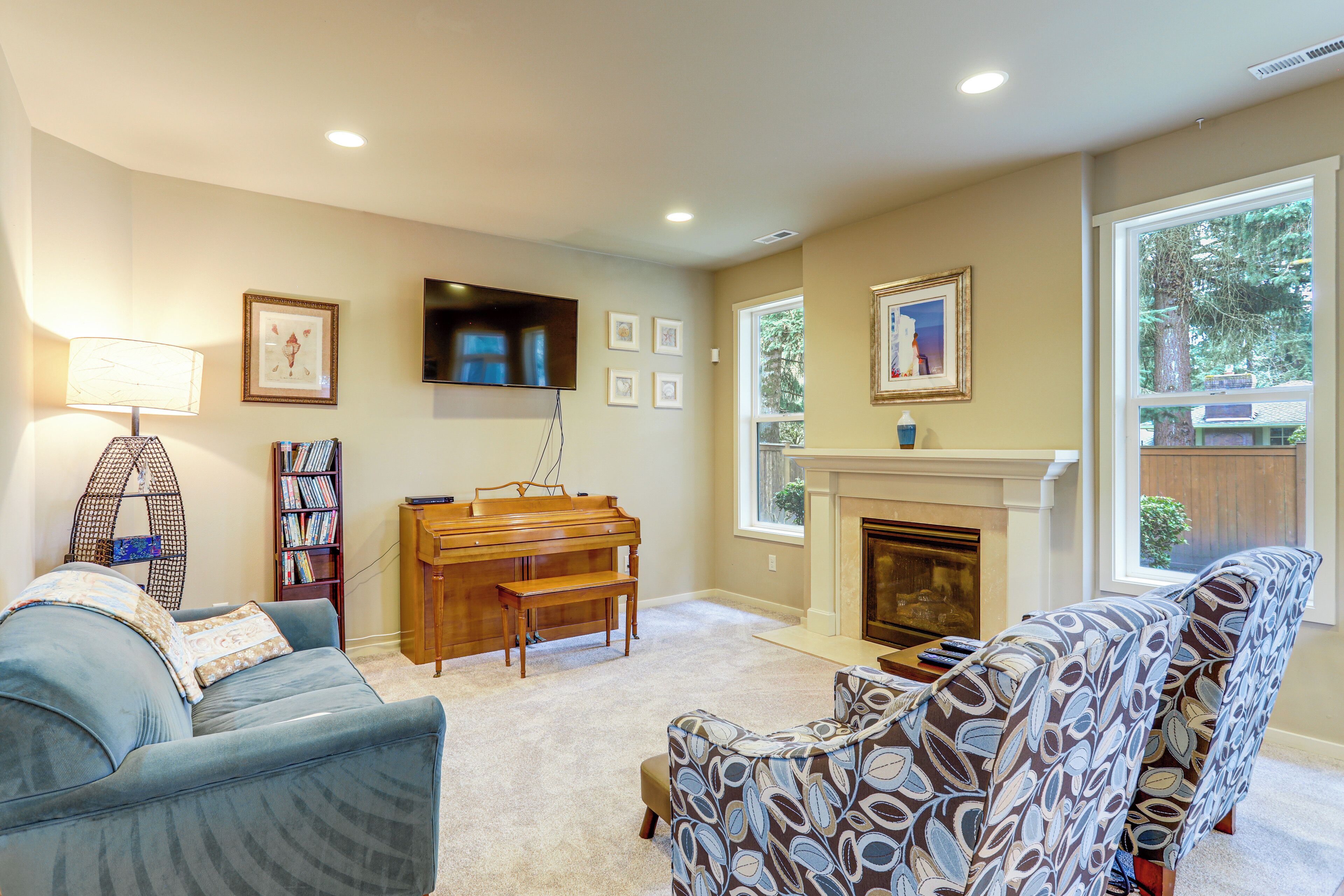 A living room with a sofa, a patterned armchair, a piano, a bookshelf, a flat-screen TV, and a fireplace.