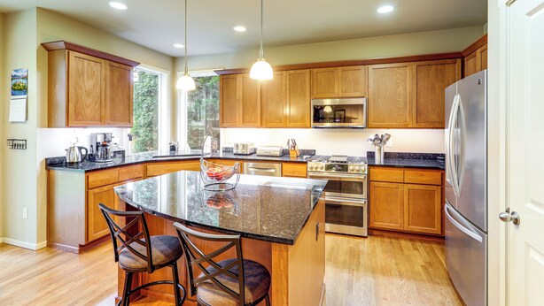 A modern kitchen with wooden cabinets, stainless steel appliances, a large island with bar stools, and pendant lighting. - Gateway to Greater Seattle! Spacious, Modern Home (Bothell)