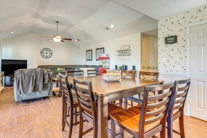 A spacious living room with a large TV, a sofa, and a dining area with wooden chairs and a table. - Hot Tub + Deck: Waterfront Lake Limestone Escape! (Jewett)