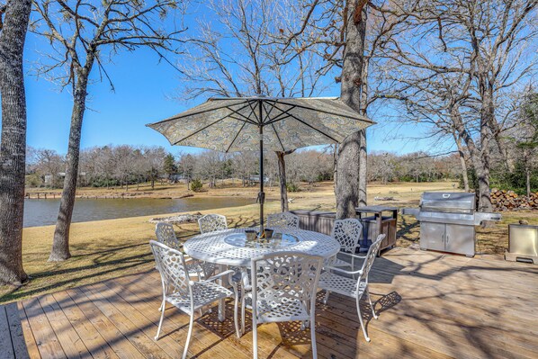 A wooden deck with a round table and chairs, an umbrella, and a grill. - Hot Tub + Deck: Waterfront Lake Limestone Escape! (Jewett)