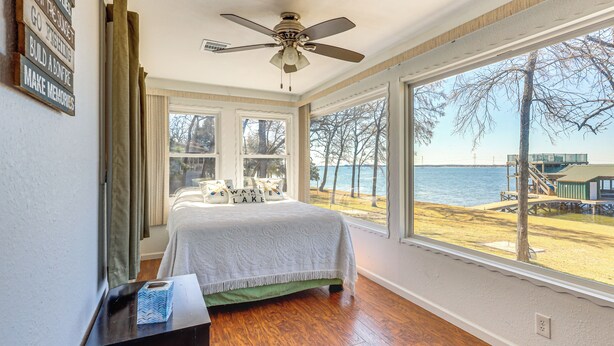 Een slaapkamer met een bed, een plafondventilator, een raam met uitzicht op het strand en een muur met motiverende borden.
