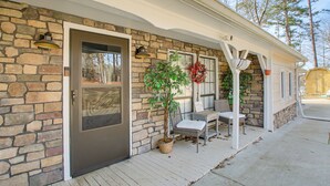 A stone exterior with a door, a covered porch with a bench, and a potted plant. - Meech Legacy House Southern Charm & Cozy Comfort (Benton)