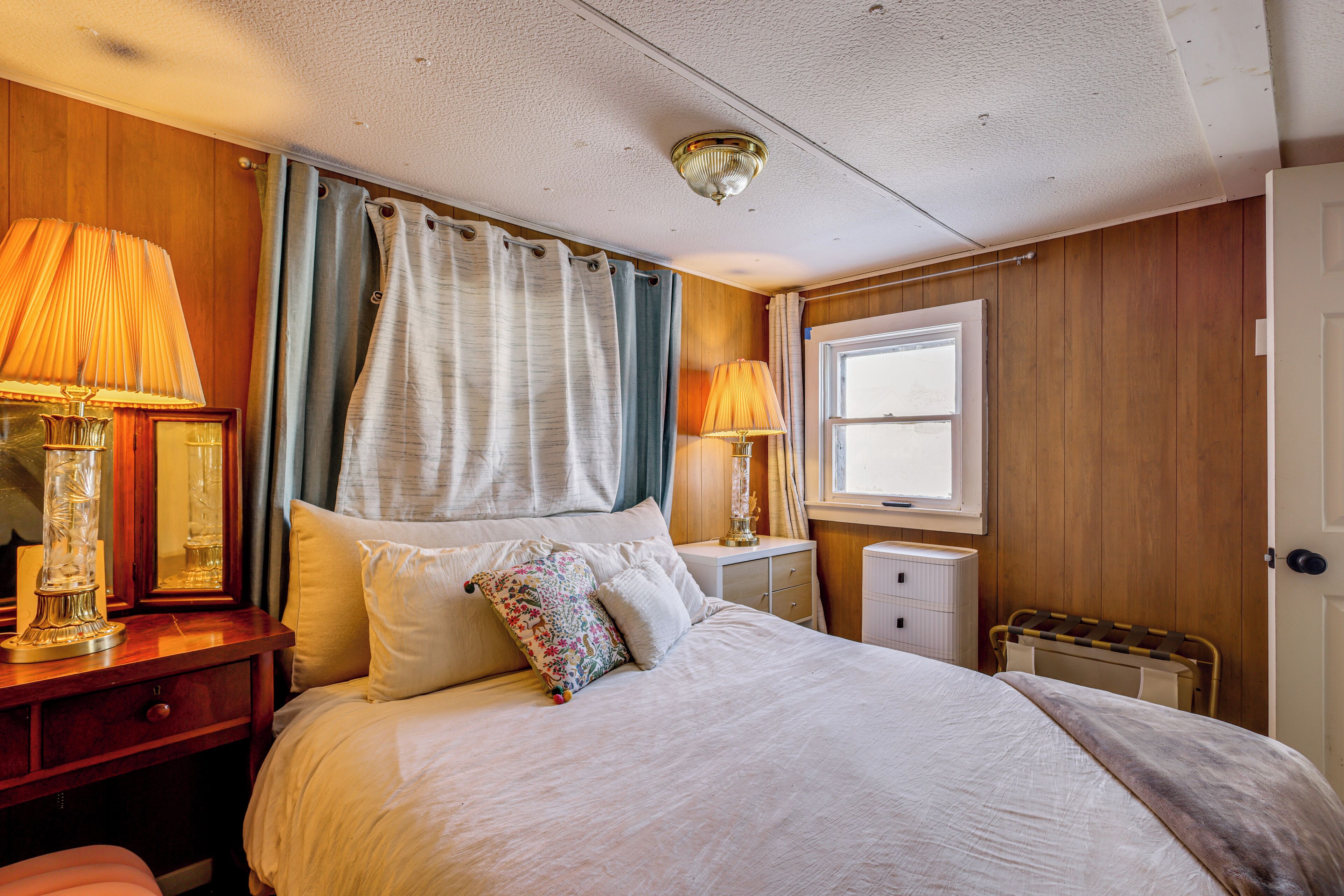 A well-lit bedroom with a large bed, two bedside tables with lamps, a window with curtains, and a radiator.