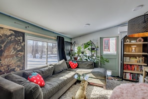 A cozy living room with a sectional sofa, a glass coffee table, a bookshelf, and a large window with a view of the outside. - < 1 Mi to Dtwn Brandon! Cozy Home w/ Fenced Yard (Brandon)