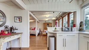 A modern kitchen with white cabinets, a wooden table, and a view of the bedroom through an open door. - 'red Barn Guest Cottage' Wine Country Escape (Sebastopol)