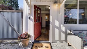 A house entrance with a red door, a welcome mat, a wicker sofa, and a potted plant. - 'red Barn Guest Cottage' Wine Country Escape (Sebastopol)