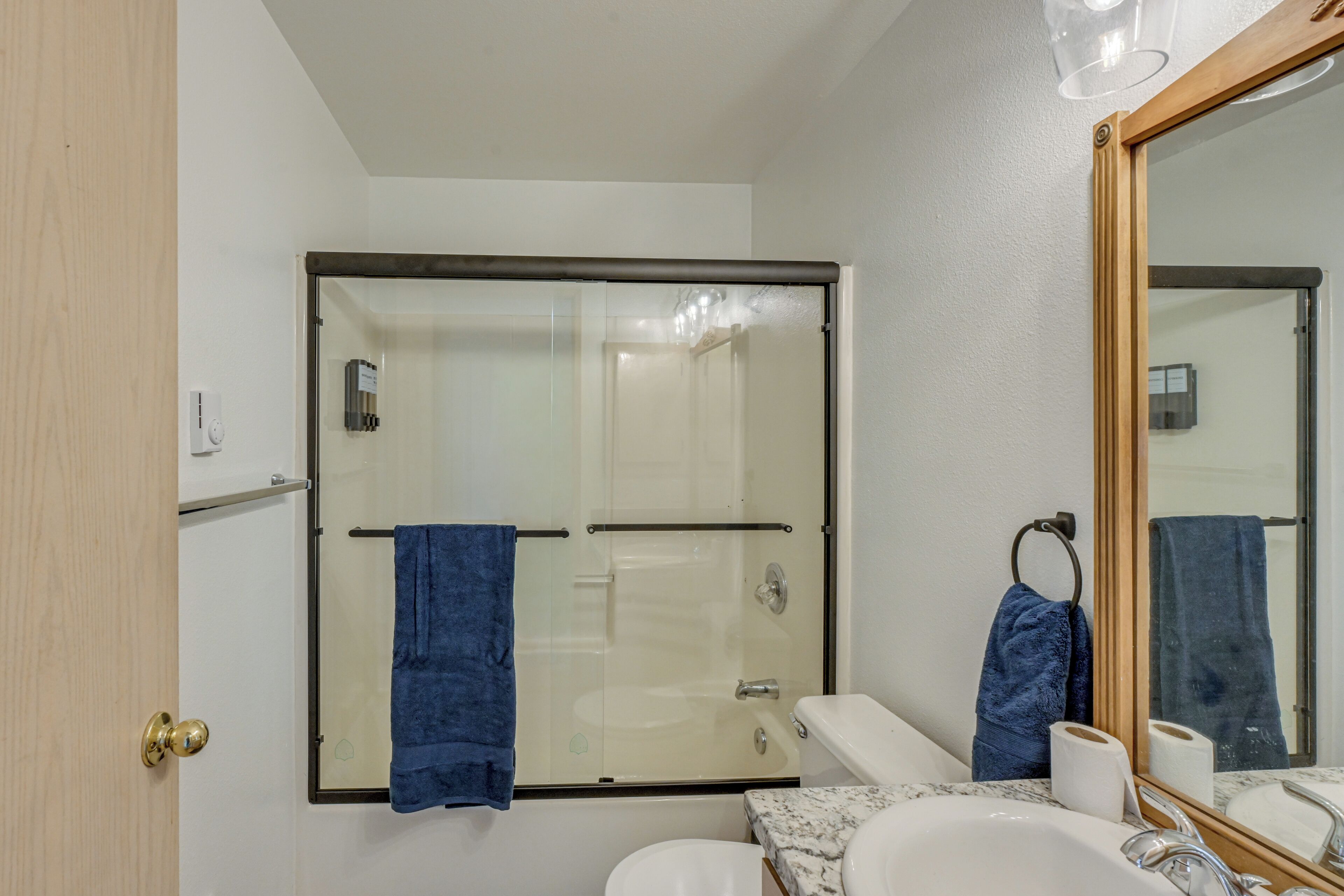 A bathroom with a glass-enclosed shower, a white toilet, a sink with a marble countertop, and a large mirror.